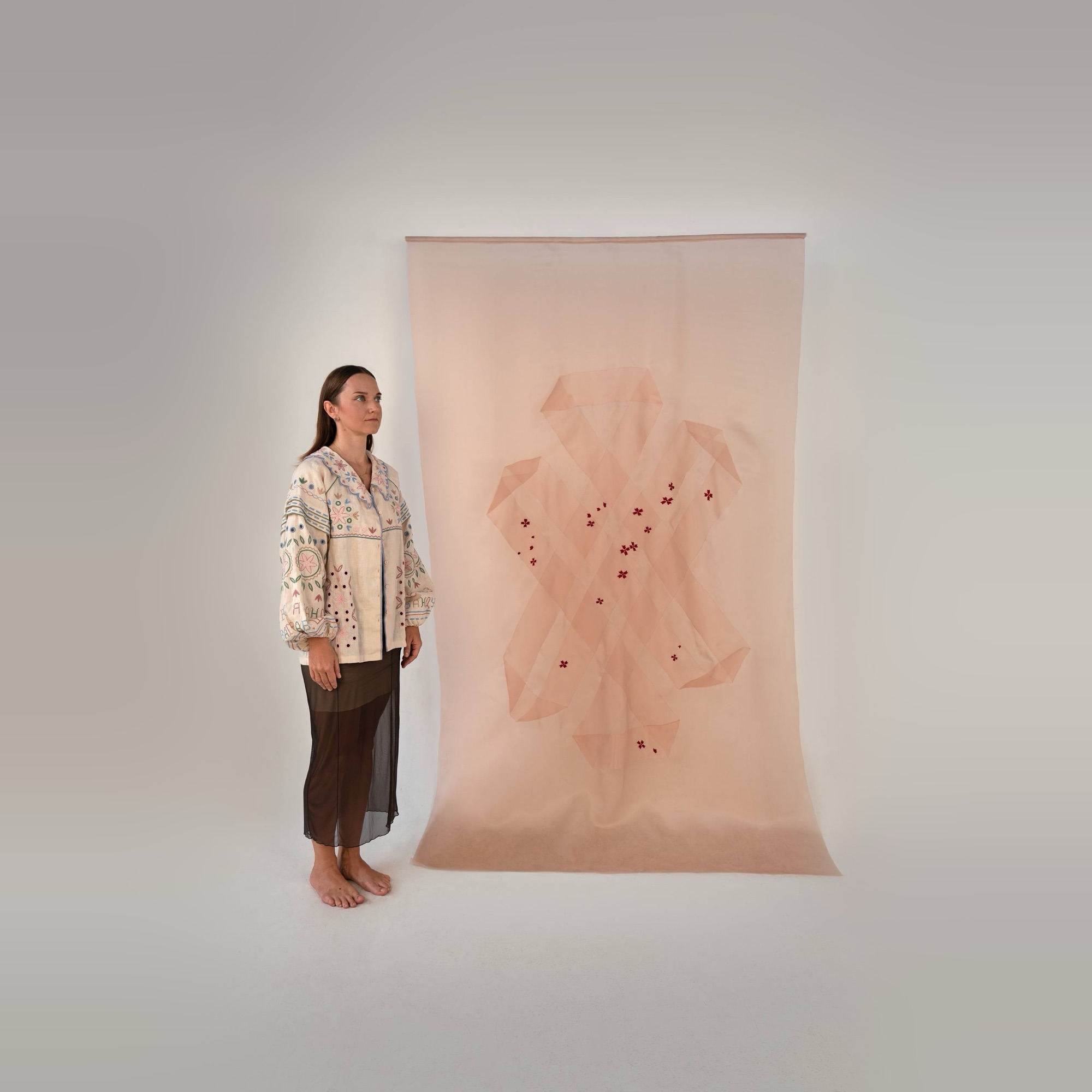 Kate Kulish in an embroidered blouse standing beside The Tibetan Knot in Ukrainian Thread